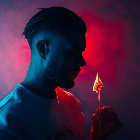 Portrait d’un homme en clair-obscur tenant une allumette enflammée, éclairé en rouge et bleu.