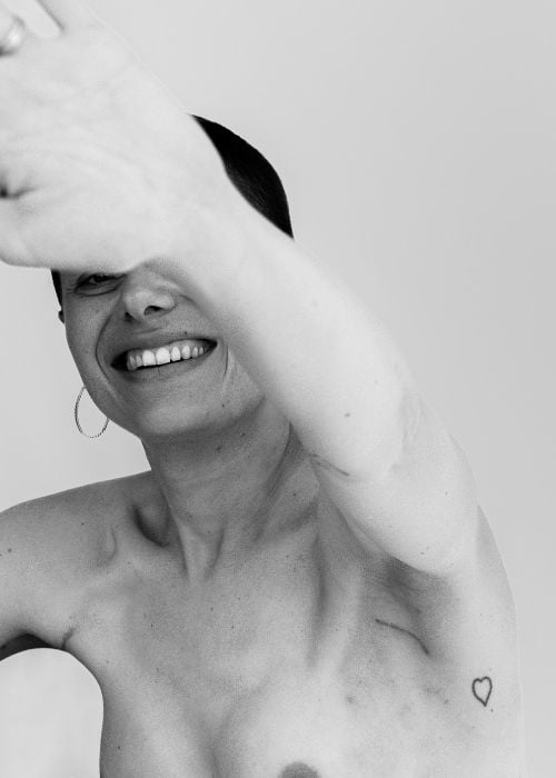 Portrait artistique en noir et blanc d’une femme souriante avec un tatouage en forme de cœur sur le bras