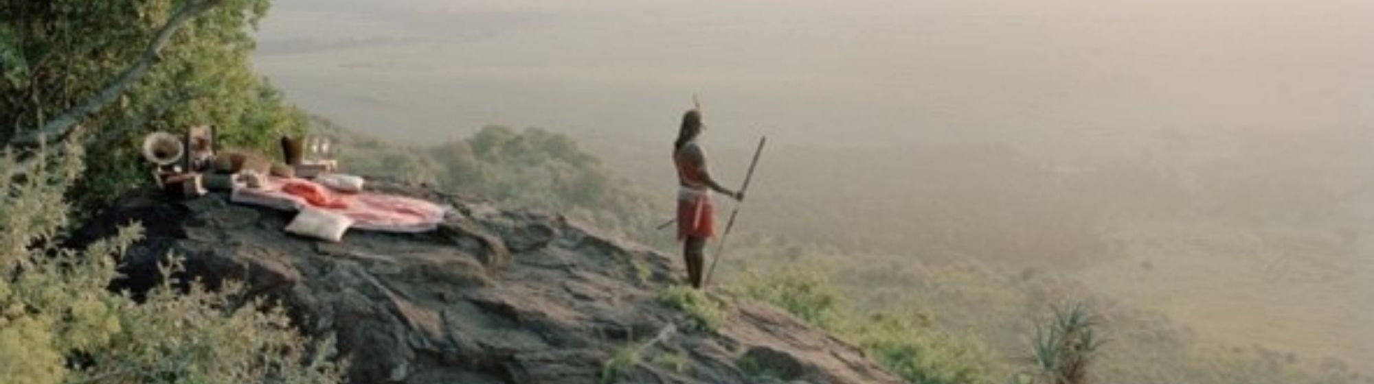 Guerrier massaï debout sur une colline, observant la savane au lever du soleil.