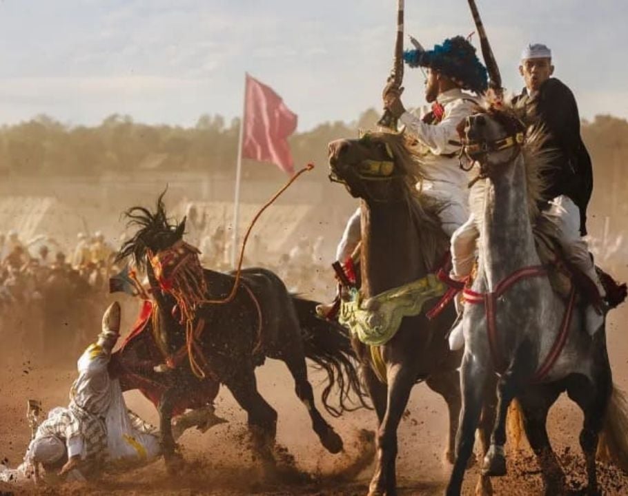 Cavaliers en pleine fantasia, l’un d’eux chute au sol dans un nuage de poussière.