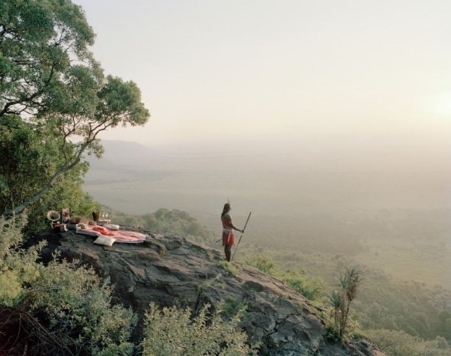 Guerrier massaï debout sur une colline, observant la savane au lever du soleil.