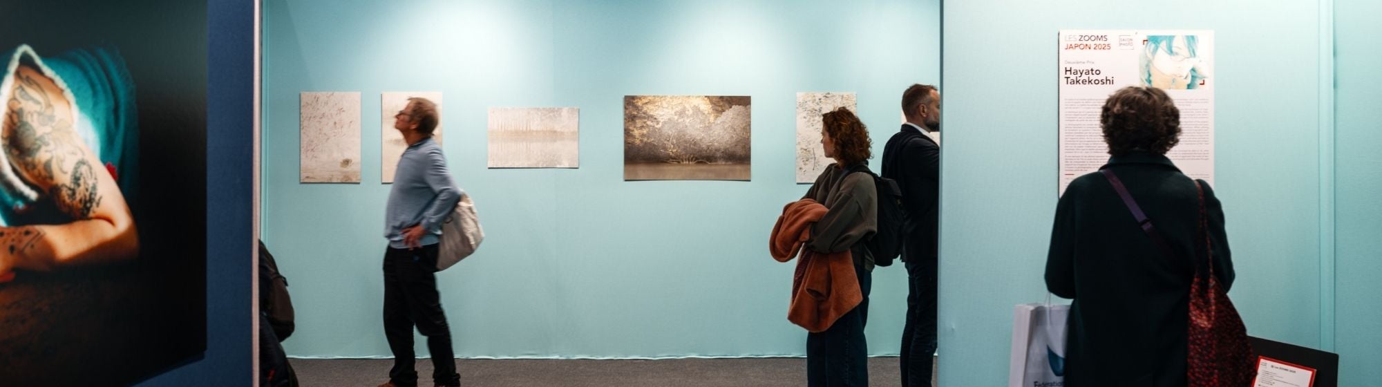Visiteurs dans une galerie d’art observant des photographies exposées sur un mur bleu clair.