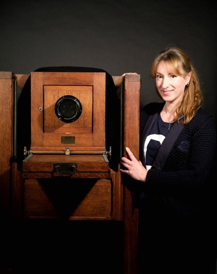 Femme posant à côté d’un appareil photo grand format ancien en studio.