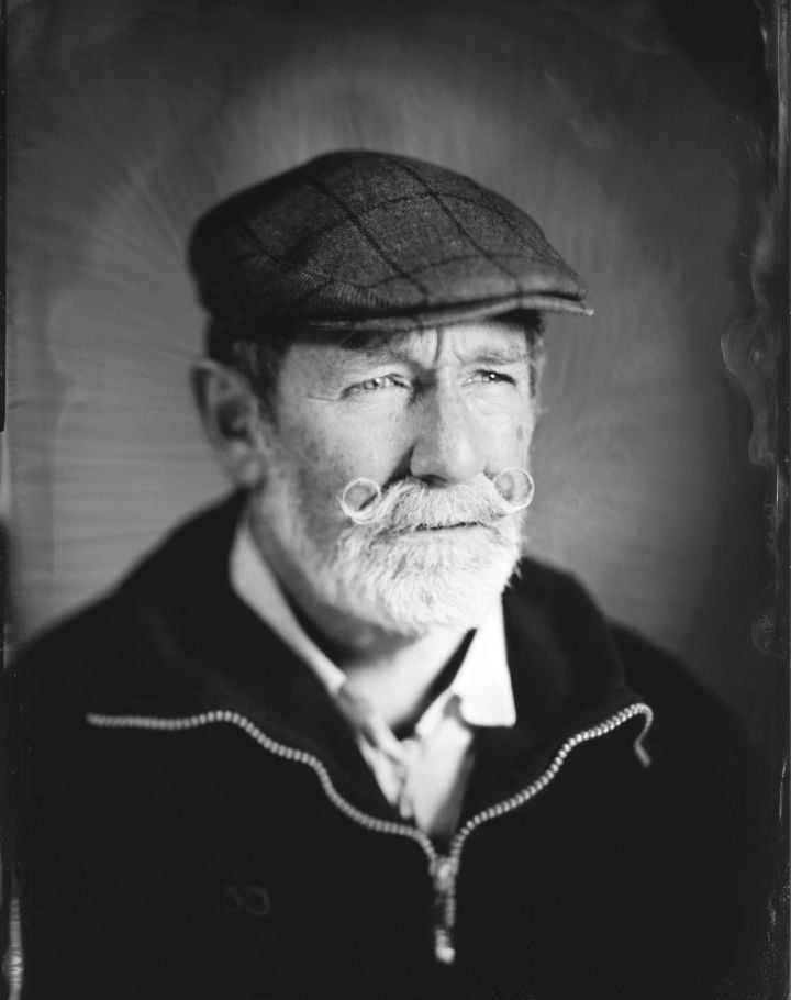 Portrait d’un homme âgé avec moustache en anneaux portant une casquette, photographié en collodion humide noir et blanc.