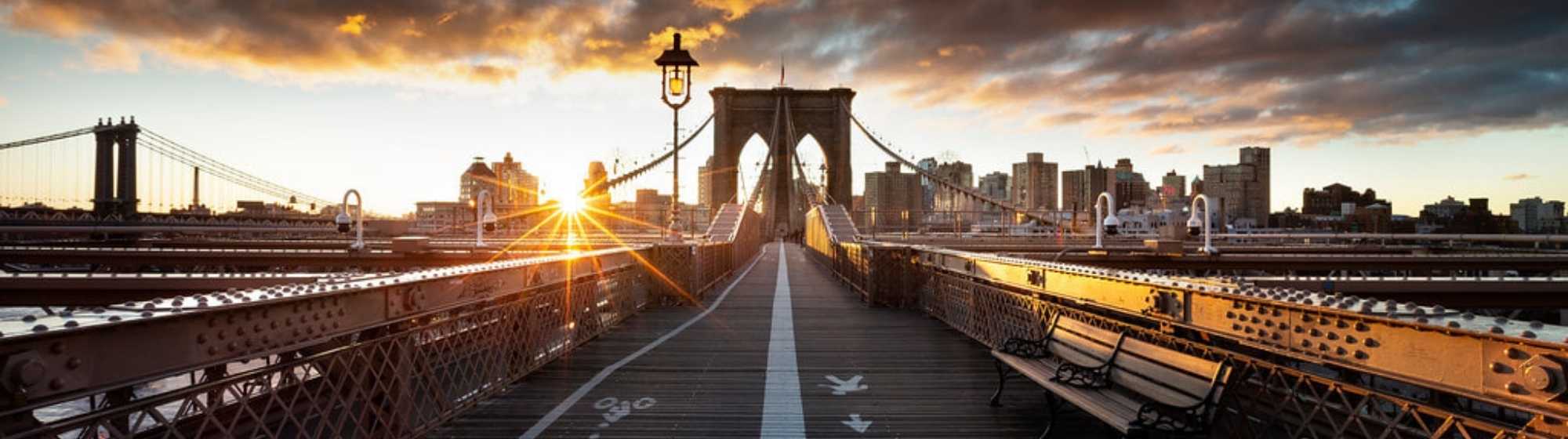 Perspective centrale du pont de Brooklyn au lever du soleil, avec des marquages piétons et cyclistes au sol.