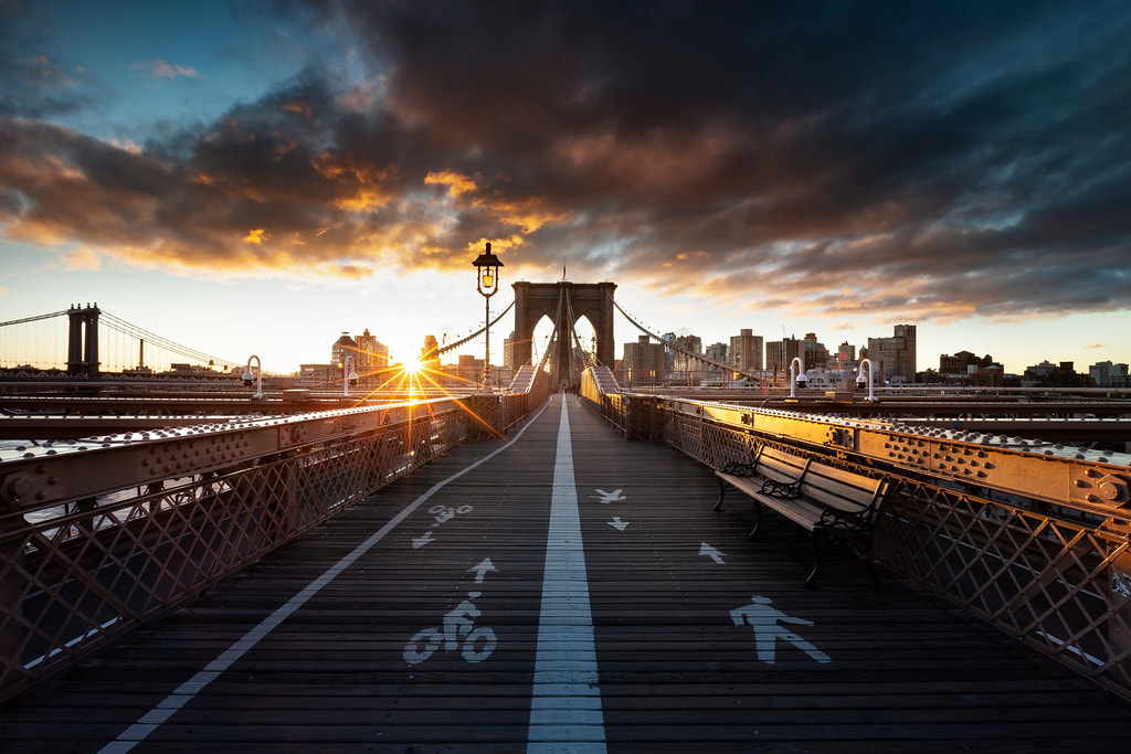 Perspective centrale du pont de Brooklyn au lever du soleil, avec des marquages piétons et cyclistes au sol.