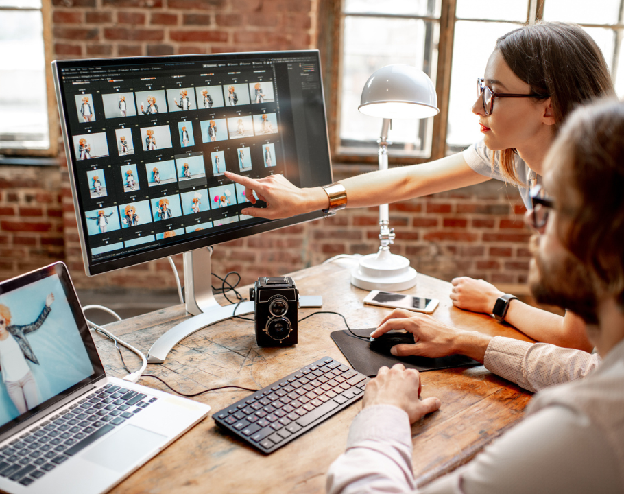Deux professionnels retouchant des photos sur un écran d’ordinateur dans un studio lumineux à murs en briques.