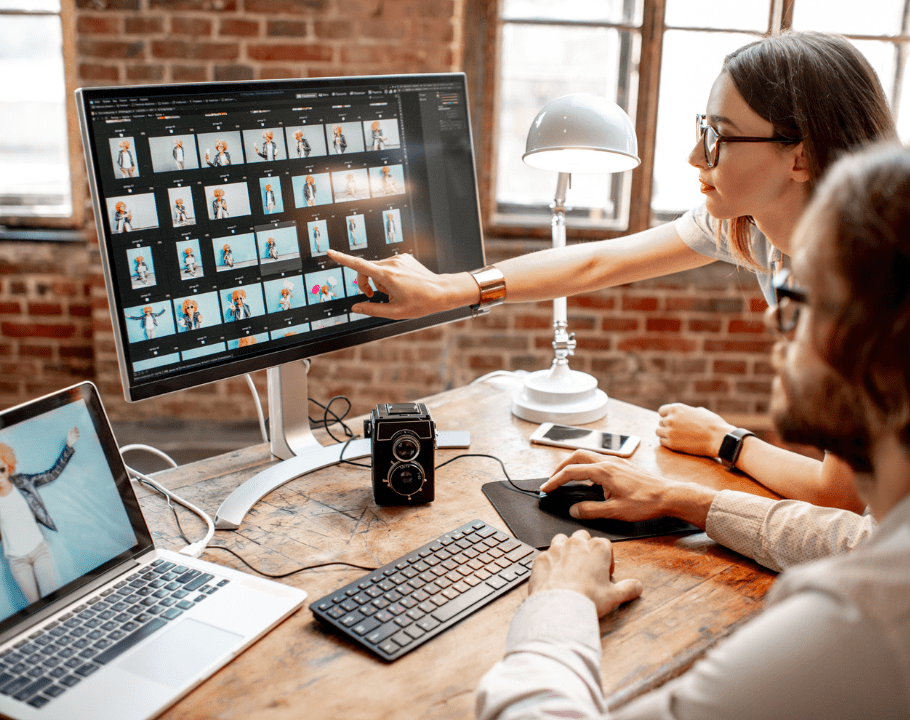 Deux professionnels retouchant des photos sur un écran d’ordinateur dans un studio lumineux à murs en briques.