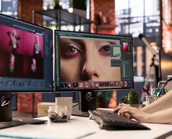 Photographe travaillant sur l'édition de photos sur des écrans d'ordinateur dans un espace de travail moderne, avec des images de modèle en gros plan affichées sur les deux écrans.