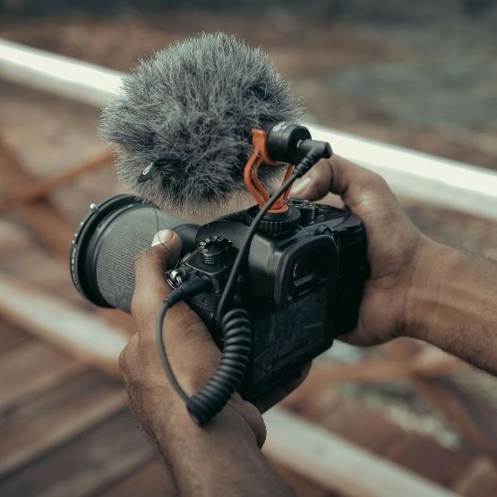 Mains tenant un appareil photo équipé d’un micro externe à bonnette, prêt à filmer en extérieur.