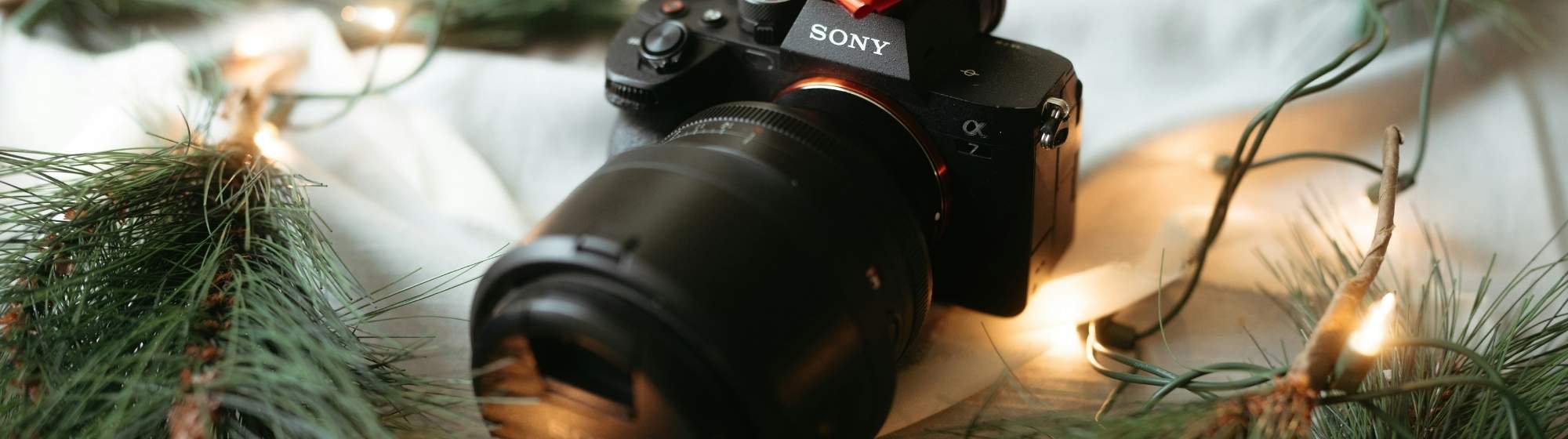 Appareil photo Sony décoré d’un nœud rouge, entouré de branches de sapin et de guirlandes lumineuses de Noël.