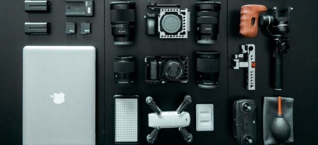 Ensemble de matériel de photographie et de vidéo organisé sur une surface noire : objectifs, drone, appareil photo et ordinateur portable.