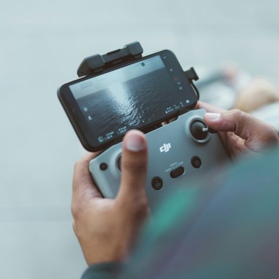 Personne tenant une radiocommande DJI connectée à un smartphone affichant la vue aérienne filmée par le drone