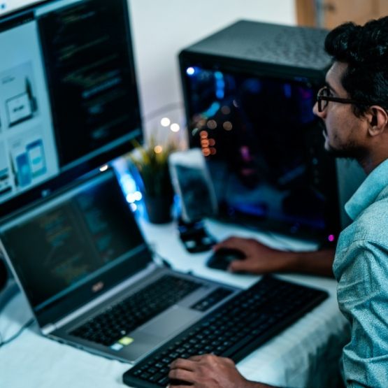 Personne utilisant plusieurs écrans d'ordinateur portable et de bureau pour coder.