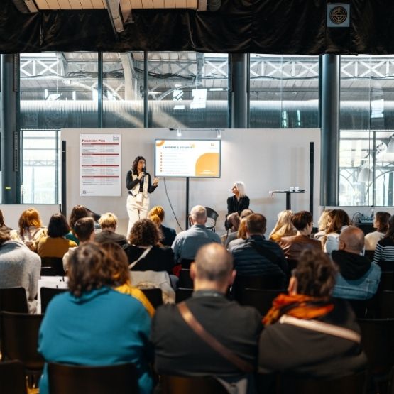 Conférence en salon avec une intervenante parlant devant un public assis.