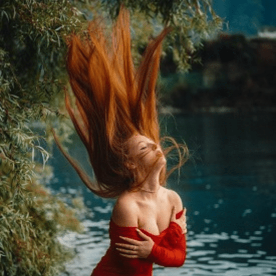 Une femme en robe rouge au bord de l'eau, sa chevelure rousse en l'air