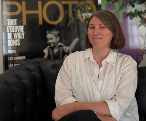 Portrait de Cyrielle Gendron, Directrice de la rédaction du Magazine Photo, assise sur un canapé noir, souriante, avec des magazines Photo en arrière-plan