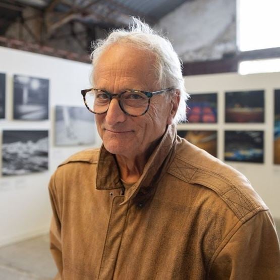 Portrait de David Burnett, photographe, souriant, dans une exposition avec photos en arrière-plan