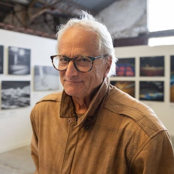 Portrait de David Burnett, photographe, souriant, dans une exposition avec photos en arrière-plan