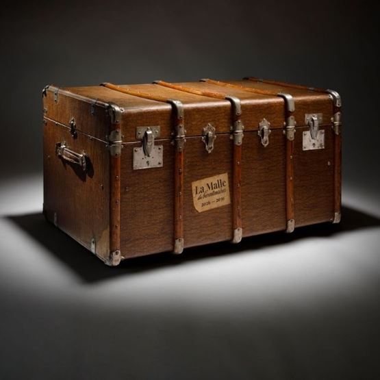 Ancienne malle de voyage en bois avec renforts métalliques et fermoirs, présentée sur un fond sombre.