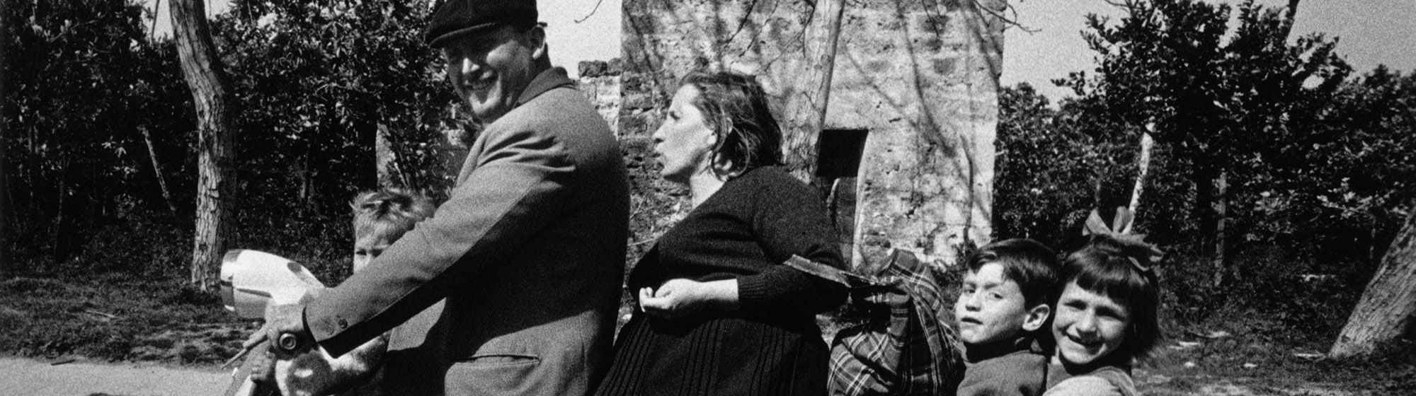 Famille nombreuse assise sur un scooter dans une rue, photographie noir et blanc vintage.