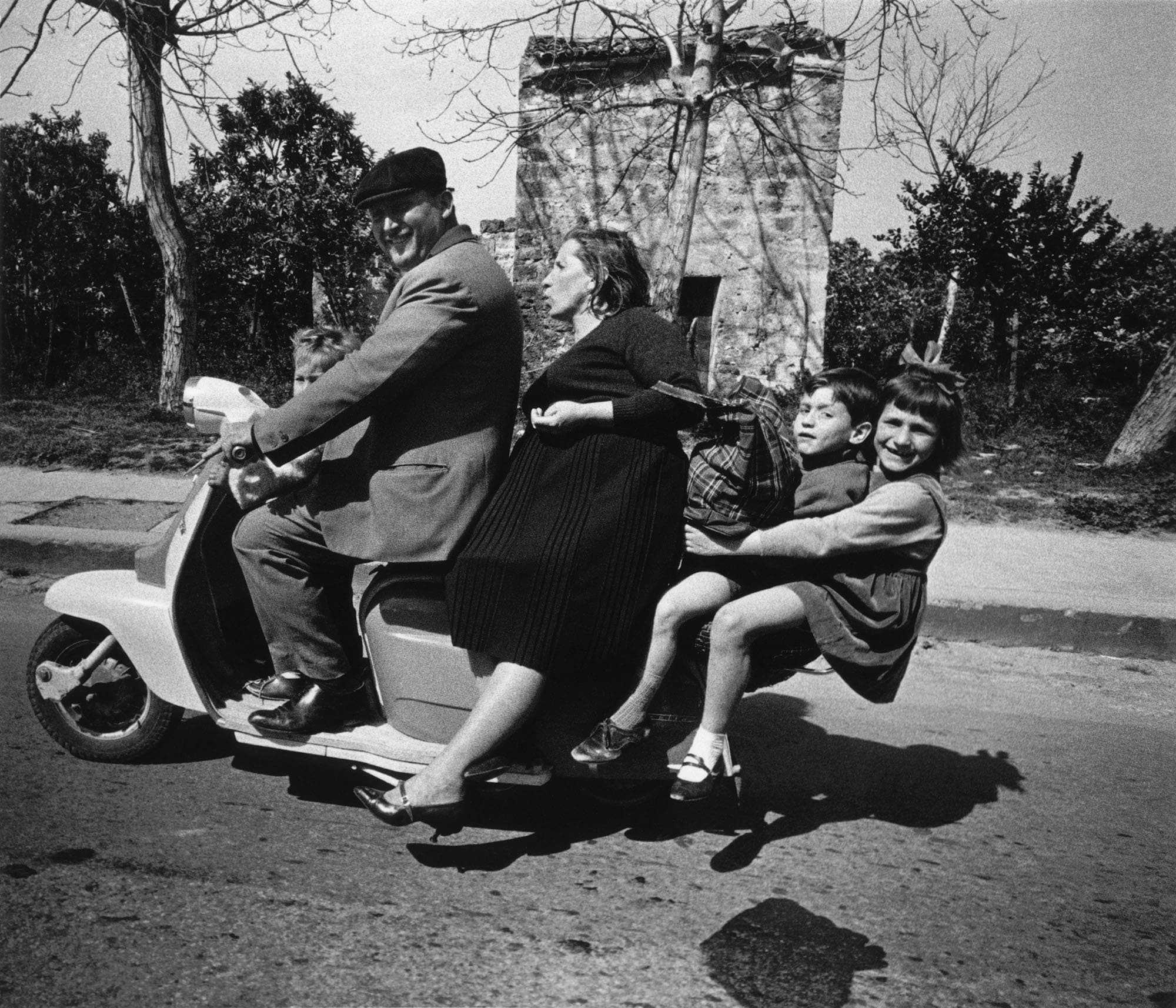 Famille nombreuse assise sur un scooter dans une rue, photographie noir et blanc vintage.