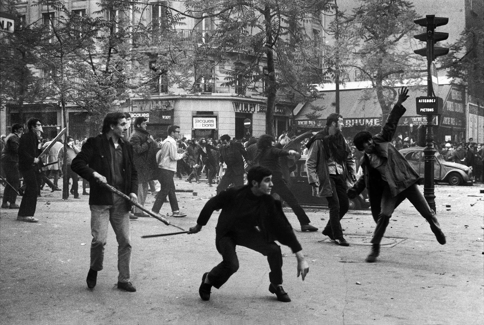 Manifestants lançant des projectiles lors d’affrontements dans une rue de ville, photographie noir et blanc.