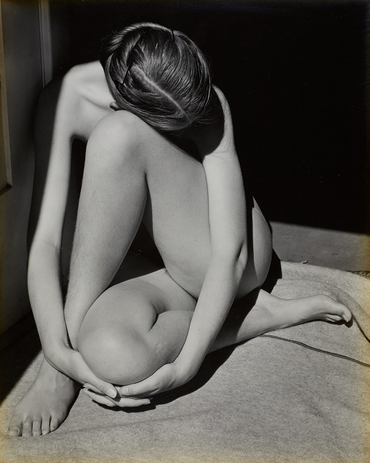Photographie artistique en noir et blanc d’un corps féminin assis, replié sur lui-même, jouant avec les lignes et les ombres.