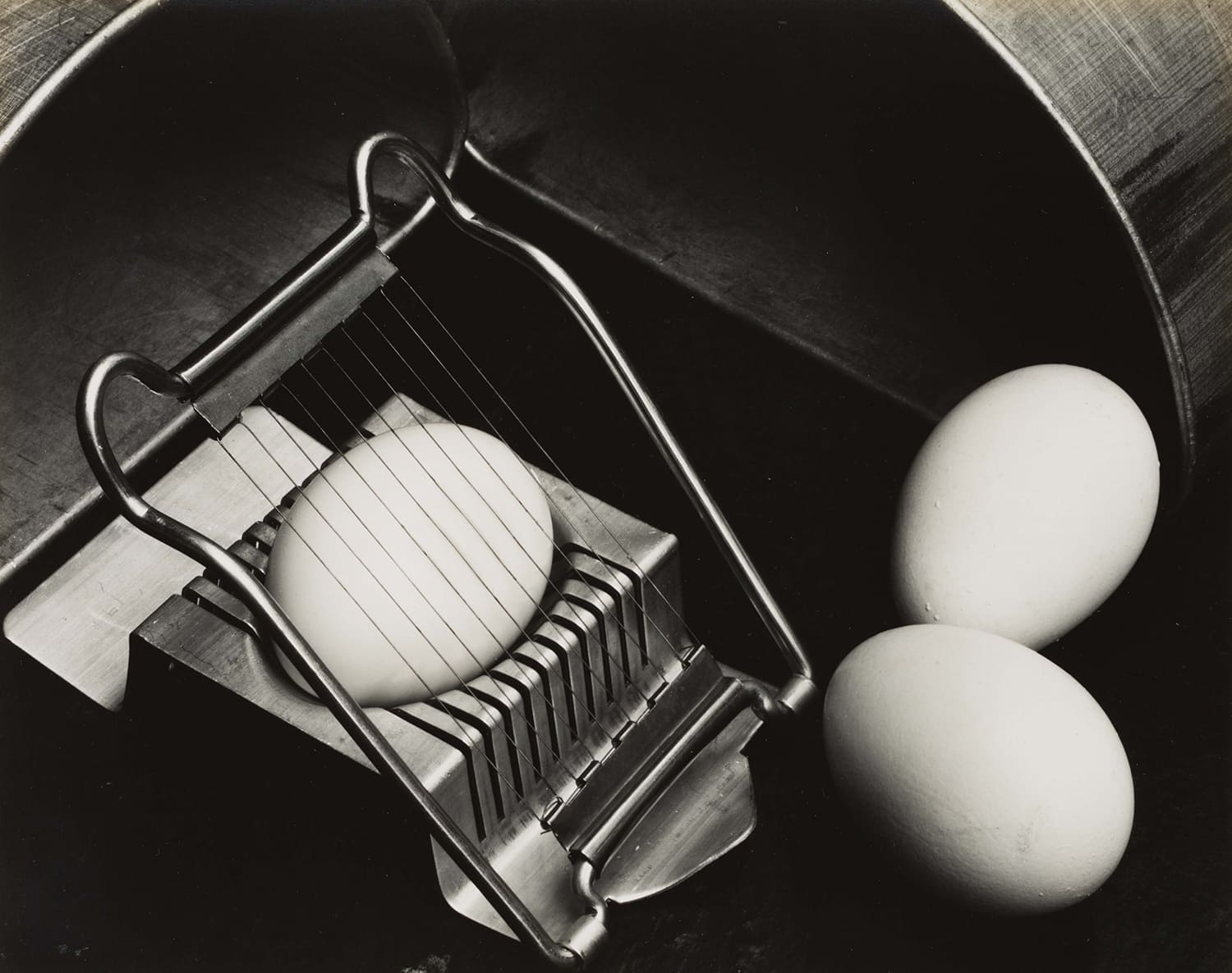 Œufs et coupe-œuf métallique photographiés en noir et blanc, nature morte à la composition géométrique.