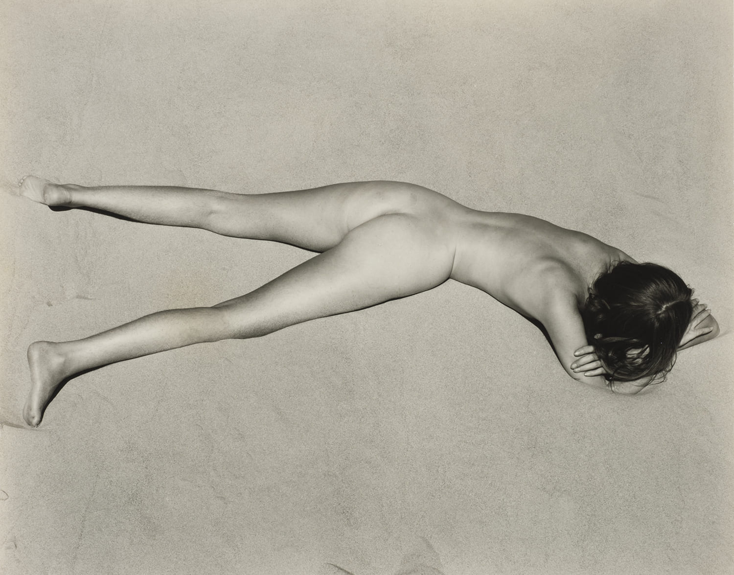 Photographie en noir et blanc d’un corps féminin allongé sur le sol, vue de dessus, composition minimaliste et graphique.