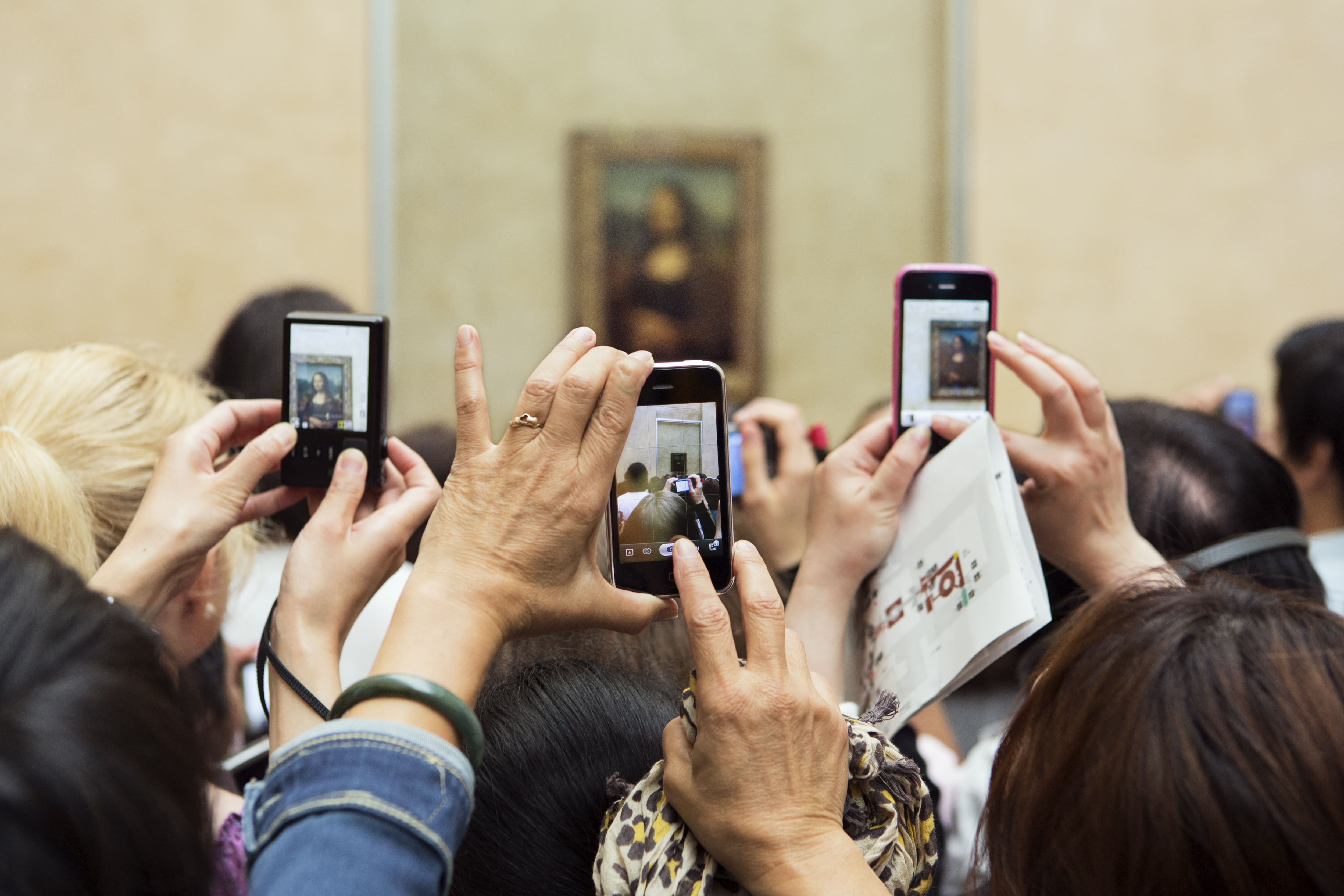 Gros plan de plusieurs mains tenant des téléphones pour prendre des photos de la Mona Lisa au Musée du Louvre.