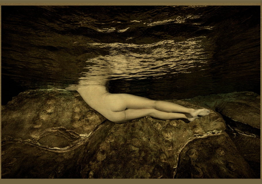 Image d'une femme nue, dos aux rochers, dans l'eau, dans les tons jaunes
