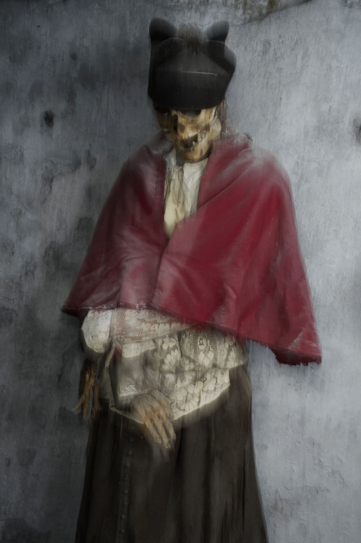 Momie de Capucin avec un voile rouge, vêtue d'un manteau en laine, capturée dans un éclairage flou.