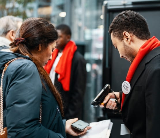 Agent de Salon de la Photo avevc un echarpe rouge et une scanner parlant à une visiteuse  