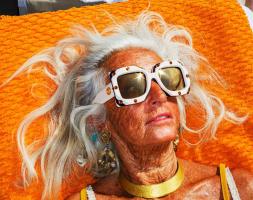 Une femme bronze avec des lunettes de soleil sur une serviette orange